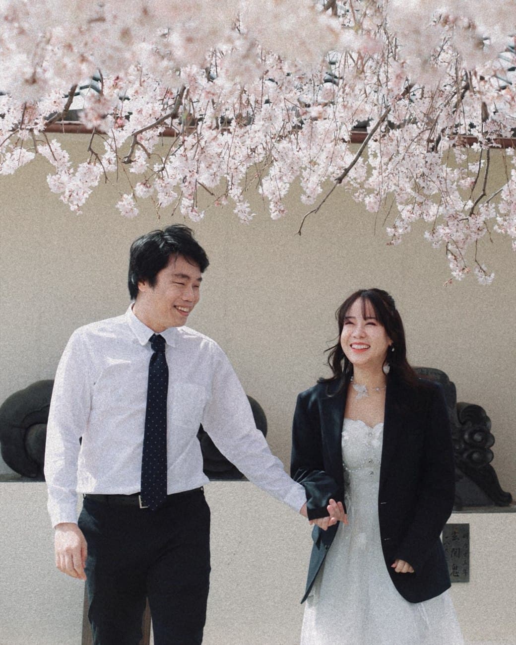 Sorratat and Witita walking hand in hand under cherry blossoms