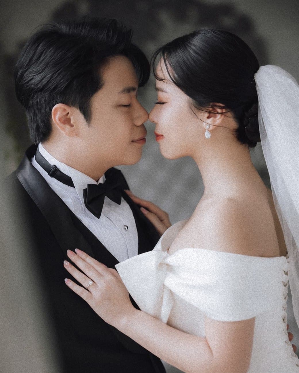 Sorratat and Witita nose to nose, eyes closed, she in a white gown and veil, he in a black tuxedo
