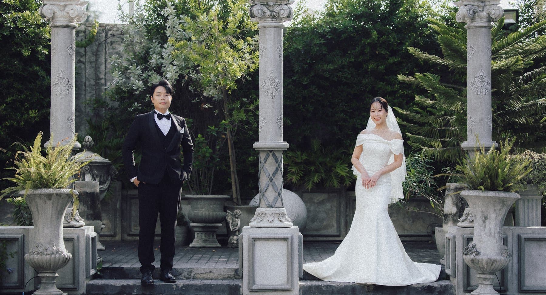 Sorratat and Witita standing apart in a courtyard of stone columns and urns